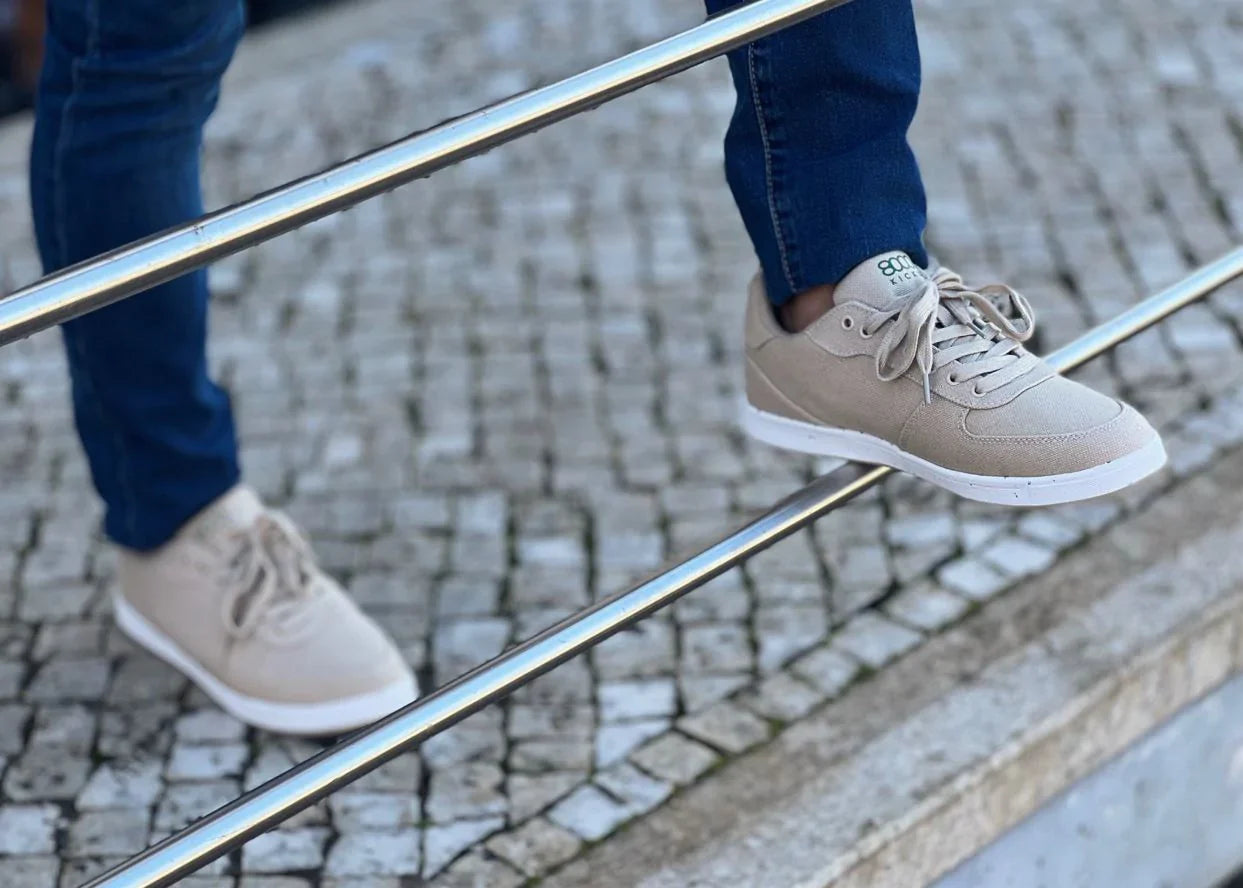 A man in blue jeans poses on a metal rail-guard with his beige hemp shoes.